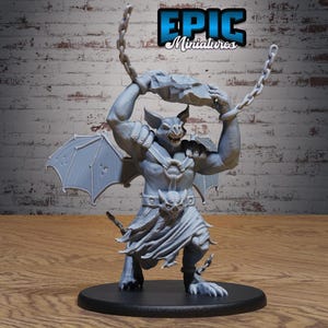 May include: A gray miniature figure of a winged bat-like creature holding a large rock above its head with chains attached to its wrists. The figure wears a loincloth with a bat-head belt buckle and stands on a round black base.