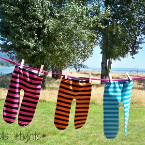 Puede incluir: Cinco pares de leggings a rayas colgados de un tendedero al aire libre. Los leggings son de varios colores, incluyendo negro, rosa, naranja, azul y arcoíris.