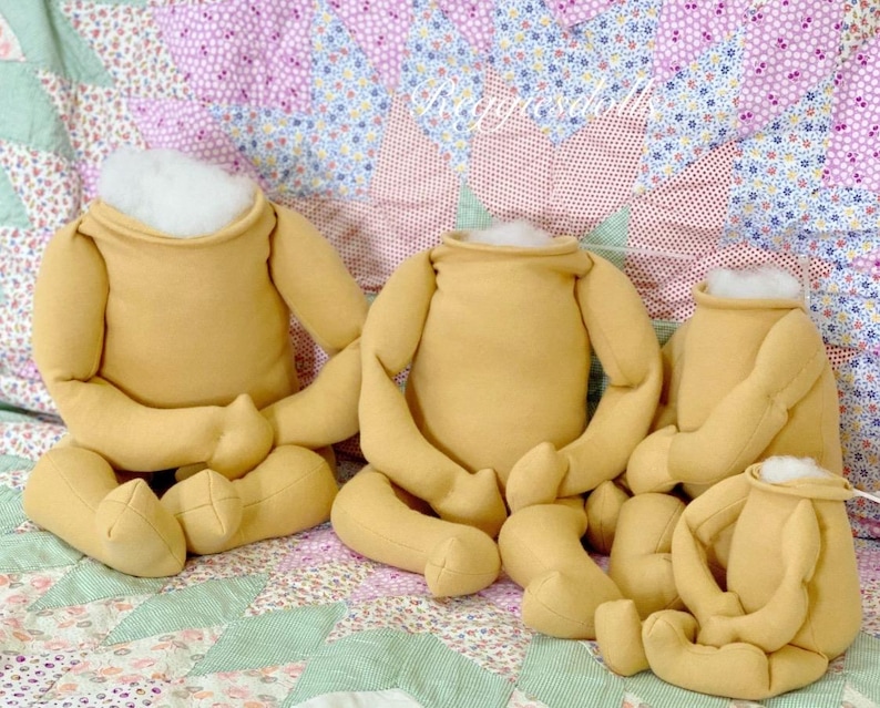 May include: Four headless, tan-colored doll bodies with arms and legs are arranged on a floral quilt. The doll bodies are stuffed with white material at the neck opening. The quilt has a patchwork design with various floral patterns.