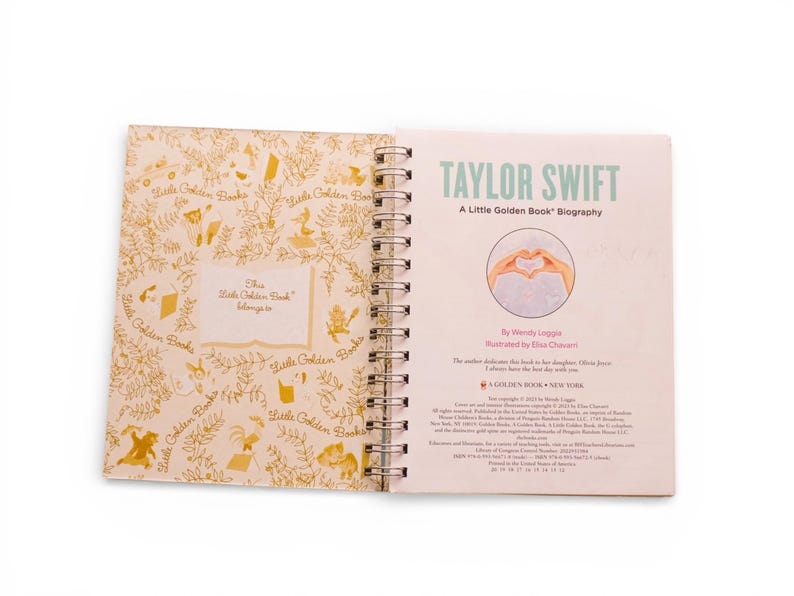 May include: Open Little Golden Book biography of Taylor Swift. The cover features the title in green and a heart-shaped hand gesture illustration. The inside cover has a gold floral pattern and the text "This Little Golden Book belongs to".