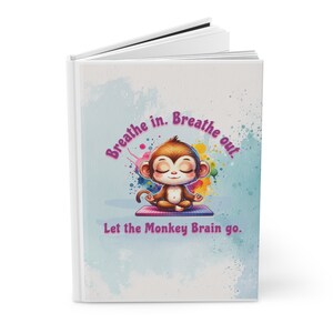 May include: A white journal with the text "Breathe in. Breathe out. Let the Monkey Brain go." features a cartoon monkey meditating. The journal has a watercolor background with colorful paint splatters.