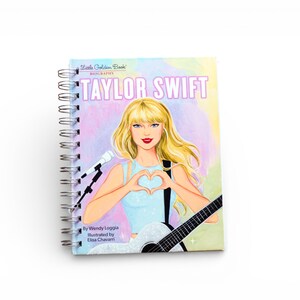 May include: A spiral-bound notebook featuring a colorful illustration of Taylor Swift. The cover displays the text "Taylor Swift Biography" with an image of the singer holding a guitar and forming a heart shape with her hands.