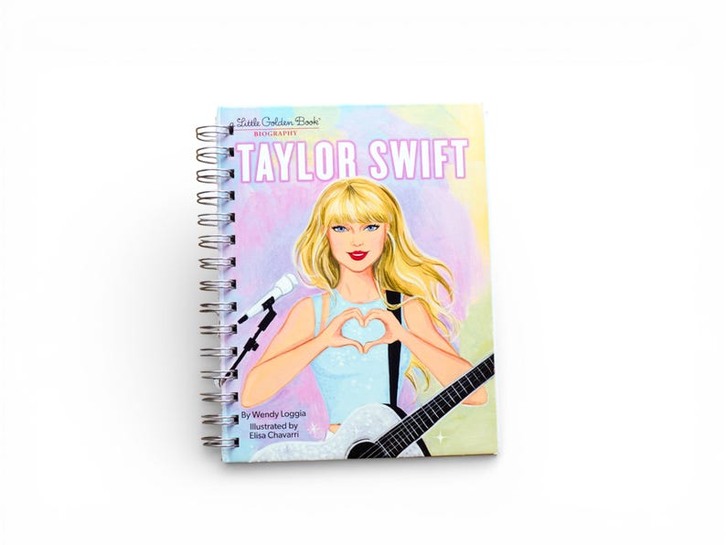 May include: A spiral-bound notebook featuring a colorful illustration of Taylor Swift. The cover displays the text "Taylor Swift Biography" with an image of the singer holding a guitar and forming a heart shape with her hands.