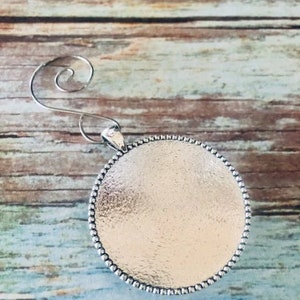 May include: Silver ornament with a round, textured surface and a beaded edge. The ornament has a wire hanger for hanging.
