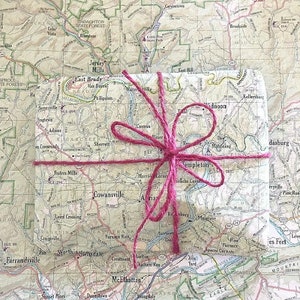 May include: A small, square package wrapped in a vintage map with a pink ribbon tied around it. The map shows the area around Cowansville, Maryland.