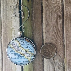 May include: A silver ornament featuring a map of Italy with the text "ITALY" in large letters. The ornament is round and has a beaded border. The map shows major cities and geographic features.