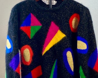 May include: Black sweater with a colorful geometric design. The sweater features shapes in red, yellow, green, blue, and pink, with gold accents. The sweater is hanging on a wooden hanger.