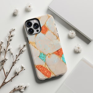 May include: A phone case with a mosaic design. The case has a cream background with sections of orange, turquoise, and gold accents. The phone case has a black camera module.