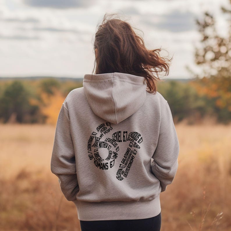 May include: A light gray hoodie with a hood, featuring a black graphic on the back with text from the Bible. The text includes "Ezekiel 6:7", "Romans 6:7", and other biblical references. The hoodie is worn by a person standing outdoors.