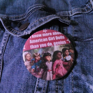 Puede incluir: Un botón redondo con el texto "I know more about American Girl Dolls than you do, genius" e imágenes de muñecas American Girl. El botón está prendido a una chaqueta vaquera azul.