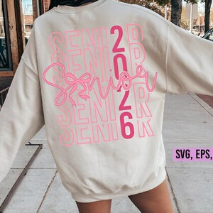 K&ouml;nnte beinhalten: Cremefarbenes Sweatshirt mit dem Wort "Senior" in rosa Schreibschrift, &uuml;berlagert vom Text "Senior 2026" in einem gestapelten, rosa Blockschrift. Das Sweatshirt enth&auml;lt auch den Text "SVG, EPS, DXF, PNG".