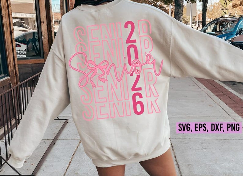 K&ouml;nnte beinhalten: Cremefarbenes Sweatshirt mit dem Wort "Senior" in rosa Schreibschrift, &uuml;berlagert vom Text "Senior 2026" in einem gestapelten, rosa Blockschrift. Das Sweatshirt enth&auml;lt auch den Text "SVG, EPS, DXF, PNG".