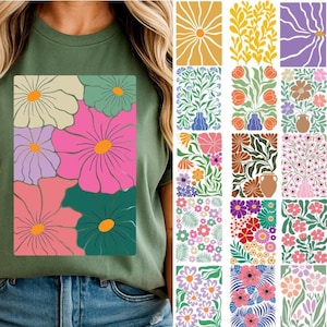 Può includere: T-shirt verde oliva con un design floreale con grandi fiori colorati in rosa, verde, viola e crema. Il design ha un centro arancione. Ulteriori motivi floreali sono visualizzati a destra.