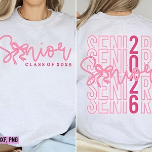 K&ouml;nnte beinhalten: Ein hellgraues Sweatshirt mit dem Wort "Senior" in rosa Schrift, einer rosa Schleife und "Class of 2026" auf der Vorderseite. Auf der R&uuml;ckseite steht das Wort "Senior" in Rosa wiederholt, mit den Zahlen "2026".