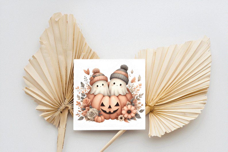 May include: A square print depicting two ghost characters in knitted hats, positioned around a carved pumpkin. The illustration uses soft watercolour tones of peach, grey, and cream, with floral accents. The print is set against a neutral background.