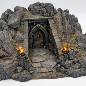 May include: A miniature fantasy diorama of a stone entrance to a cave or dungeon. The entrance is framed by large gray rocks and lit by two torches. The wooden door has an arched top and a circular handle.