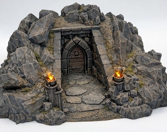 May include: A miniature fantasy diorama of a stone entrance to a cave or dungeon. The entrance is framed by large gray rocks and lit by two torches. The wooden door has an arched top and a circular handle.
