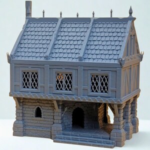 May include: A gray, unpainted miniature building featuring a stone-textured ground floor with an arched doorway and a timber-framed upper level with three lattice-style windows. The roof has a shingled texture with decorative finials along the ridge.