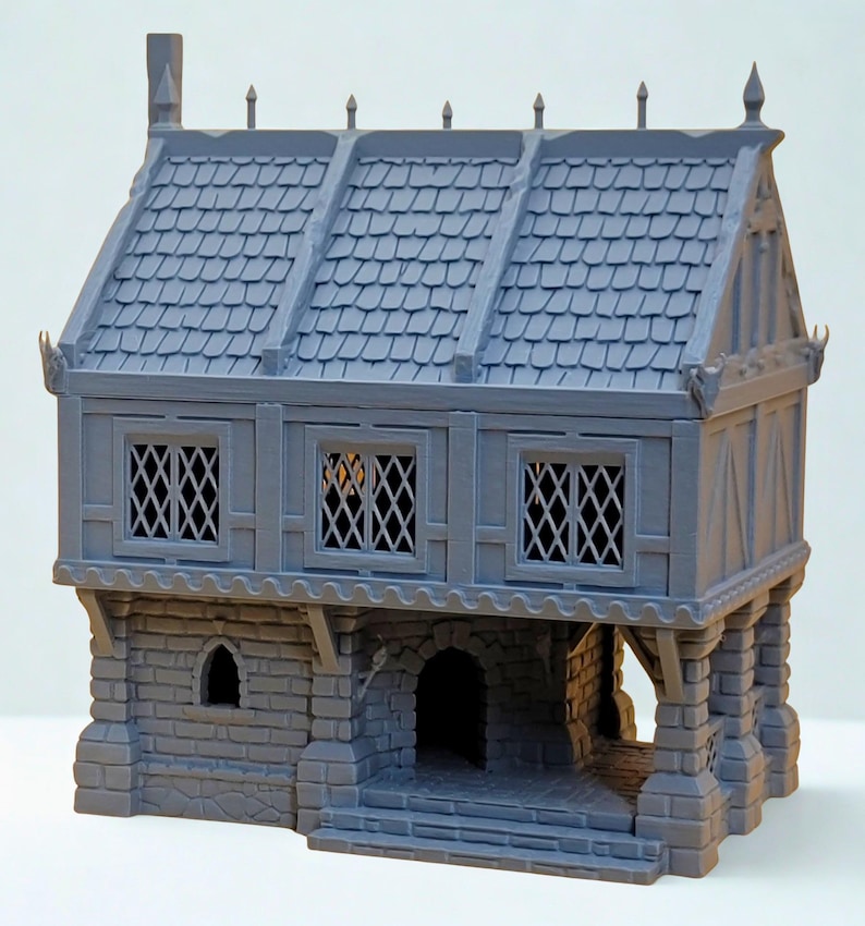 May include: A gray, unpainted miniature building featuring a stone-textured ground floor with an arched doorway and a timber-framed upper level with three lattice-style windows. The roof has a shingled texture with decorative finials along the ridge.
