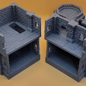 May include: Two gray, 3D-printed miniature stone building structures featuring open-concept interiors, detailed brick masonry walls, arched window cutouts, and a raised circular balcony platform on one of the structures, designed for tabletop gaming.