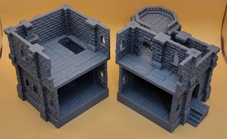 May include: Two gray, 3D-printed miniature stone building structures featuring open-concept interiors, detailed brick masonry walls, arched window cutouts, and a raised circular balcony platform on one of the structures, designed for tabletop gaming.