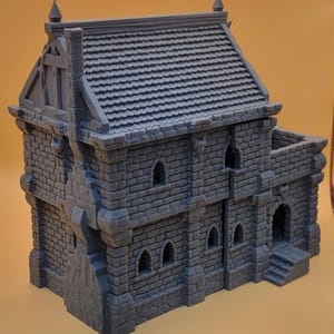 May include: A gray 3D printed miniature building featuring a detailed stone brick texture, a tiled roof, a prominent chimney, and multiple arched windows. The structure includes a small entrance with steps and a flat-topped section on the side.