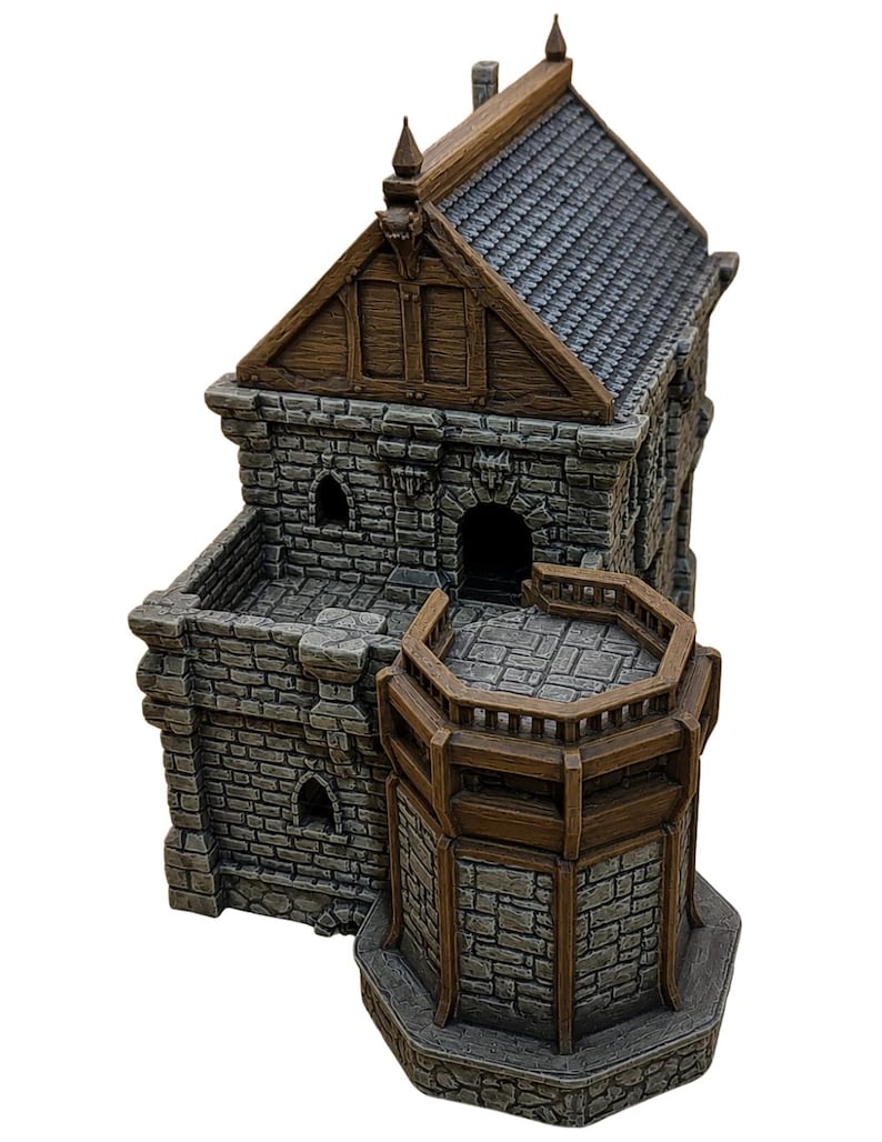 May include: A miniature stone building featuring gray brick walls, a brown wooden roof with dark shingles, and a wooden balcony. The structure includes arched doorways, small windows, and a multi-level design with a prominent hexagonal tower section.