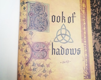 May include: An open book with a vintage, parchment-like cover. The title "Book of Shadows" is written in a gothic font with a triquetra symbol. The year "1693" is written below the title.