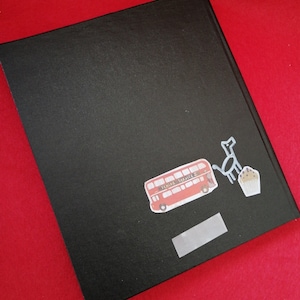 May include: Black hardcover journal with a red double-decker bus, a black dog, and a cupcake sticker on the front. The bus sticker says "Senior Service".