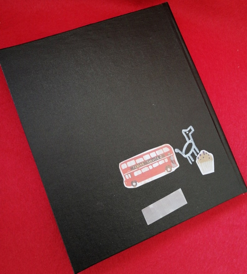 May include: Black hardcover journal with a red double-decker bus, a black dog, and a cupcake sticker on the front. The bus sticker says "Senior Service".