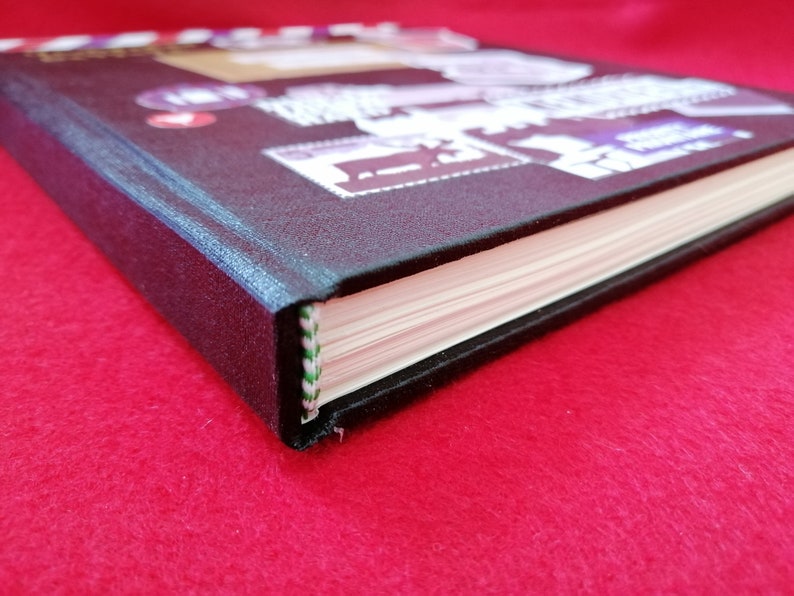 May include: A black hardcover journal with a decorative cover featuring colorful stamps and a red heart. The journal has a white spine with green and white stitching.