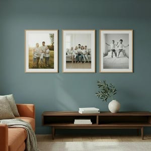 May include: Three rectangular picture frames with light wood borders are mounted on a dark teal wall. Each frame contains a different photograph of a family, including outdoor portraits and indoor scenes, displayed in a horizontal row.