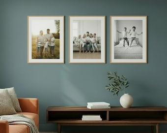 May include: Three rectangular picture frames with light wood borders are mounted on a dark teal wall. Each frame contains a different photograph of a family, including outdoor portraits and indoor scenes, displayed in a horizontal row.