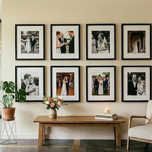 May include: Eight framed black and white wedding photographs are displayed on a cream-colored wall. A wooden bench with a floral arrangement and a candle sits below the photos. A potted plant and a chair with a blanket are also in the room.