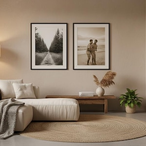 May include: A modern living room with neutral tones, featuring a cream-colored sectional sofa, a wooden coffee table, and a round jute rug. Two framed black and white photographs hang on the wall above the sofa. A fireplace with a burning fire adds warmth.