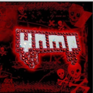 May include: A red and white enamel pin with the word "YUMMM" spelled out in white letters with red glitter. The pin is surrounded by red rhinestones.
