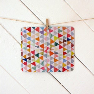 May include: A colorful card with a geometric pattern of triangles in shades of red, orange, yellow, green, blue, and purple. The card is hanging from a string with a wooden clothespin.