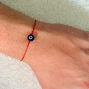 Puede incluir: Una pulsera de cuerda roja con un dije azul de ojo turco.