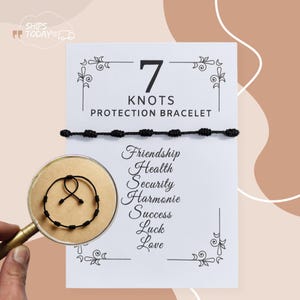 Op de afbeelding: Een zwart 7 Knots Protection Bracelet wordt getoond op een witte kaart met de woorden "7 Knots Protection Bracelet". De kaart bevat ook de woorden "Vriendschap, Gezondheid, Veiligheid, Harmonie, Succes, Geluk, Liefde". Een vergrootglas toont een close-up van de armband.