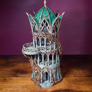 May include: A detailed miniature tower made of gray stone with a green roof and vines growing up the sides. The tower has a balcony and a small door at the base.