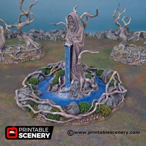 May include: A detailed miniature fantasy fountain with a statue of a robed figure, a waterfall, and a pool of blue water. The fountain is surrounded by rocks, green foliage, and tree roots. The scene is set in a natural environment with bare trees in the background.