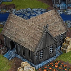 Könnte beinhalten: Ein Miniatur-Wikingerhaus aus Holz mit Strohdach. Das Gebäude hat eine dunkelbraune Holzverkleidung, ein Steinfundament und dekorative Schnitzereien. Kleine Kürbisse und Heuballen im Vordergrund deuten auf ein Erntethema hin.