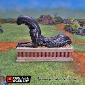 May include: A black alien creature figurine lying on a stone platform with a textured surface. The creature is in a crouching position with its head bowed. The platform is made of a light brown material and has a series of small, rectangular indentations.