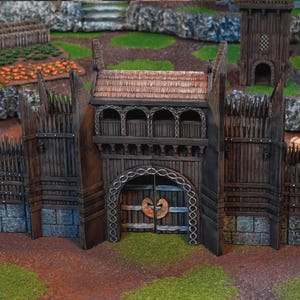May include: A detailed miniature wooden castle gate with a thatched roof, arched doorway, and decorative metalwork. The gate is flanked by tall wooden palisades and sits on a grassy surface, suggesting a fantasy or historical theme.