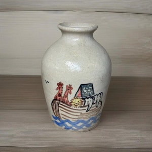 May include: A white ceramic mug with a black handle and the text "But First, Coffee" in a bold, black font. The mug is filled with a dark liquid, likely coffee, and sits on a light-colored surface.