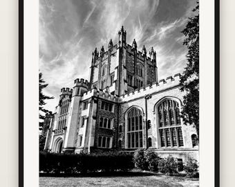 May include: A black and white framed photograph of a large stone building with gothic architectural features, including tall towers, arched windows, and crenelated rooflines, set against a sky with wispy clouds and dark trees.