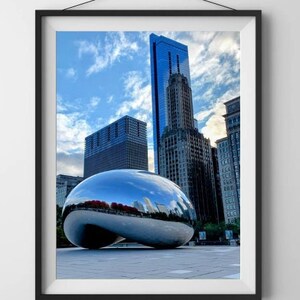 Puede incluir: Fotografía enmarcada de la escultura Cloud Gate de Chicago, una gran estructura reflectante de acero inoxidable, sobre un fondo de rascacielos y un cielo azul con nubes. La obra de arte refleja el horizonte de la ciudad.
