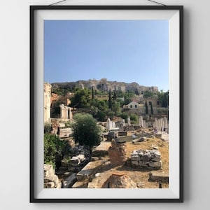 May include: A framed photograph of an ancient city with ruins in the foreground and a hilltop with buildings in the background. The sky is blue and the sun is shining.