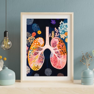 Op de afbeelding: Een ingelijste kunstdruk met een kleurrijke illustratie van longen. Het kunstwerk toont de longen in tinten oranje, roze en geel, met bloemaccenten tegen een donkerblauwe achtergrond. De print is ingelijst in een lichtgekleurde houten lijst.