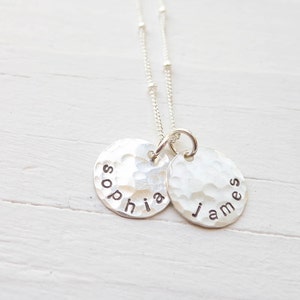 May include: Silver necklace with two hammered disc pendants, one with the name "Sophia" and the other with the name "James".
